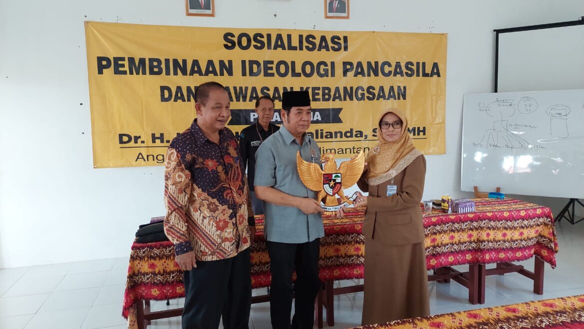 Anggota DPRD Provinsi Kalsel Dr H Karlie Hanafi Kalianda, SH MH menyerahkan Lambang Negara berupa ukiran Burung Garuda kepada Kepala SMAN 1 Tabukan Emmi Listyawati disela acara sosialisasi.(foto : ist)