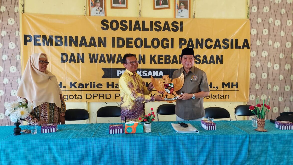 Anggota DPRD Provinsi Kalsel Dr H Karlie Hanafi Kalianda, SH, MH saat menyerahkan cindera mata berupa ukiran lambang negara Garuda Pancasila yang diterima Rusian Syah, SPd Kepala SMAN 1 Bakumpai, Kecamatan Bakumpai, Kabupaten Barito Kuala.(foto : ist)