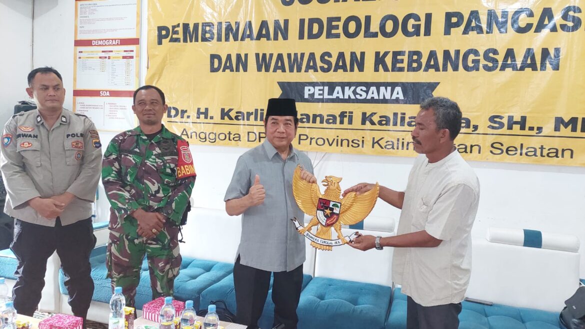 Anggota DPRD Provinsi Kalsel Dr Karlie Hanafi Kalianda, SH, MH menyerahkan cindera mata berupa ukiran Lambang Negara Garuda Pancasila yang diterima Kepala Desa Anjir Muara Kota, Khairullah, Jumat (21/7/2023).(foto : ist)