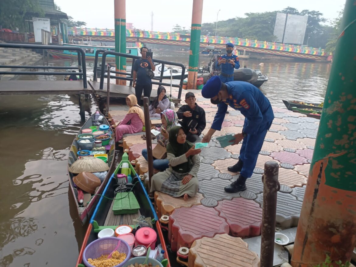 BAGI MASKER- AKP Dading Kalbu Adie selaku Kasat Polairud Polresta Banjarmasin saat membagikan masker kepada salah satu pengunjung di Pasar Terapung, Minggu (8/10/2023) pagi. (foto:ist) 
