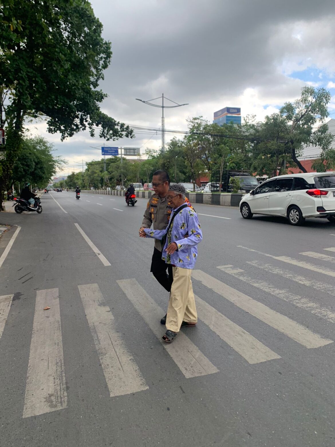 SEBERANGKAN LANSIA - Kapolresta Banjarmasin Kombes Pol Sabana Atmojo saat embantu seorang pria Lanjut Usia (Lansia)bmenyeberangkan jalan tepat di depan Mapolresta Jalan A Yani Km 3, Rabu (1/5/2024) pagi. (foto:ist)
